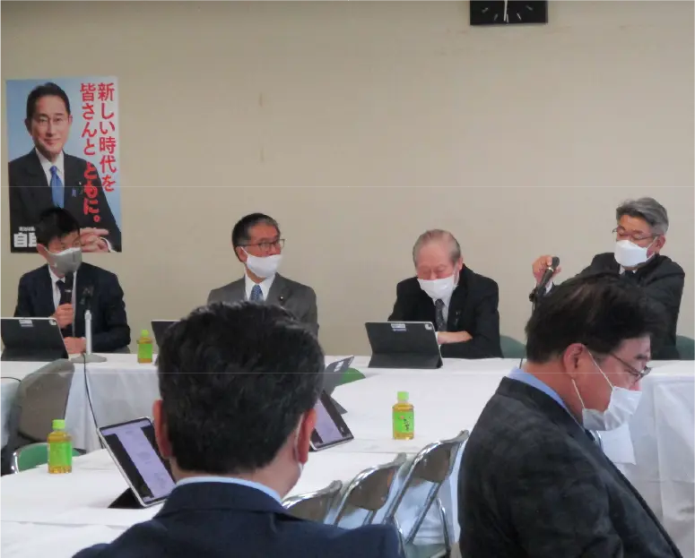自民党本部にて、災害対策特別委員会事務局長として采配を振るうかつまた孝明。会議室には他の議員が集まっている。