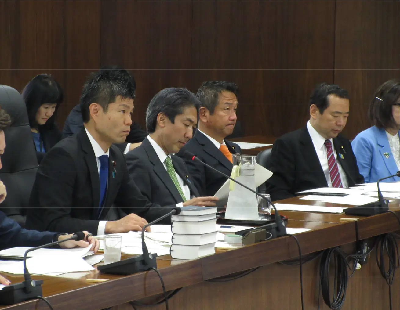 第212回臨時国会にて衆議院外務委員長に就任したかつまた孝明(画像左)が、会議に参加している様子。複数の議員が資料を手にし、真剣な表情で臨んでいる。
